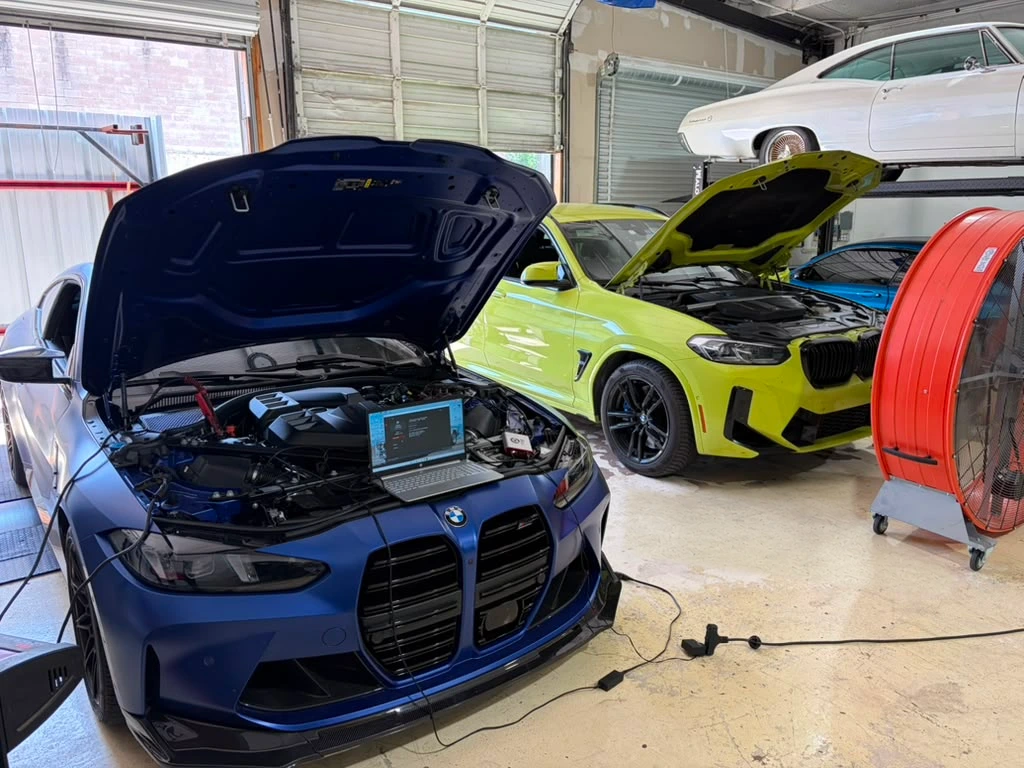 Blue and yellow BMW M cars with their hoods open in the Cedar Performance workshop