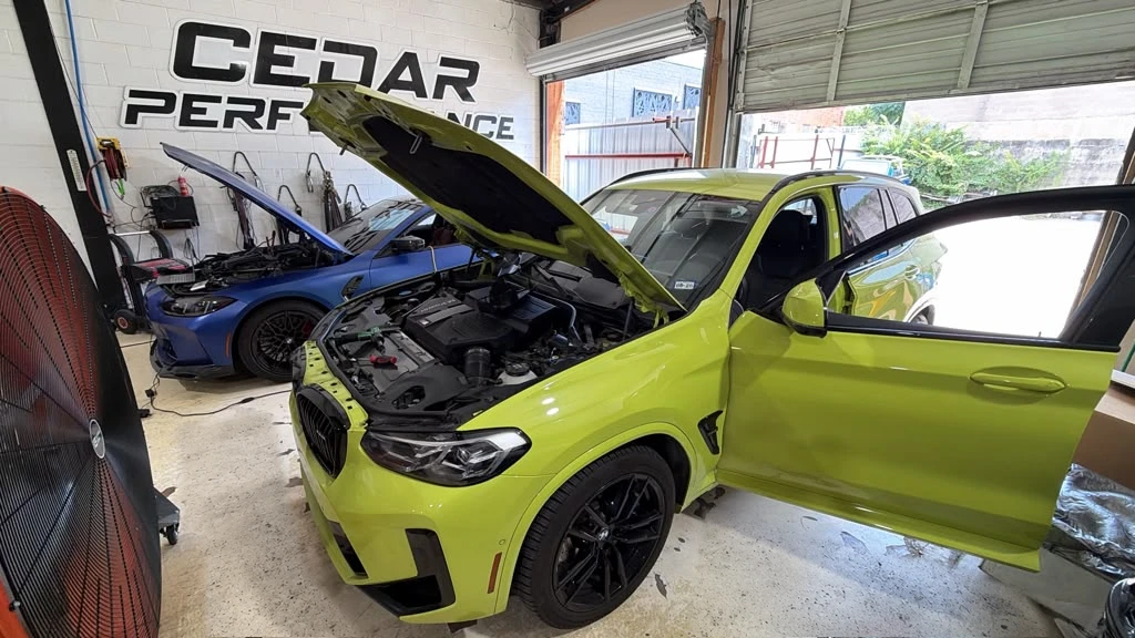 Yellow BMW performance SUV with its hood open in the Cedar Performance workshop