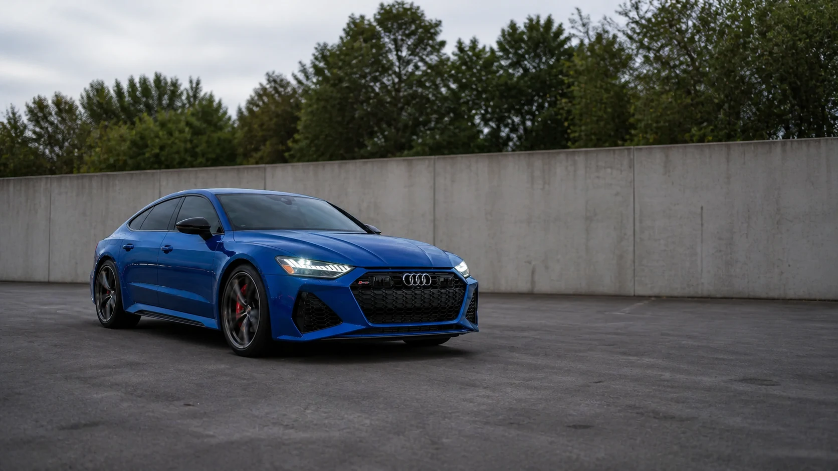 Blue C8 Audi RS7 parked beside a locality-neutral concrete wall