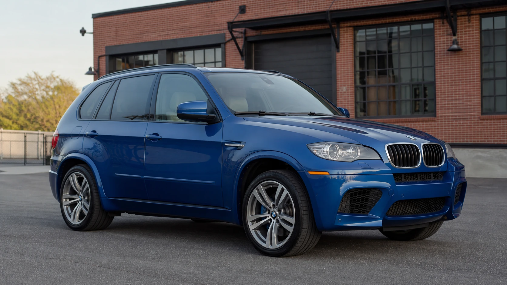 Blue E70 BMW X5 M outside a brick industrial shop