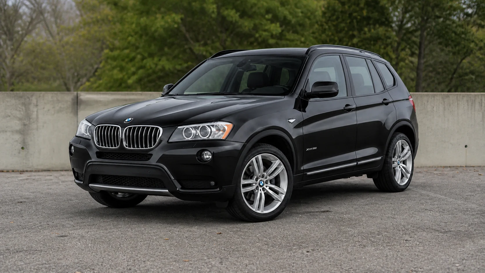 Black F25 BMW X3 beside a low concrete wall
