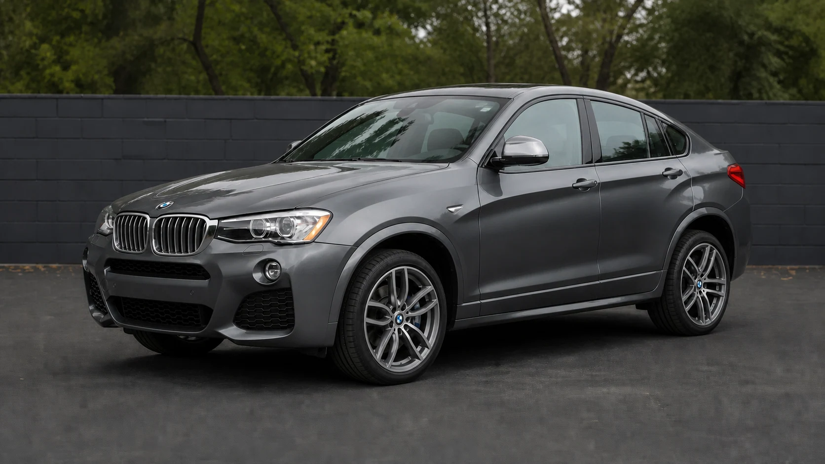 Dark gray F26 BMW X4 beside a charcoal masonry wall