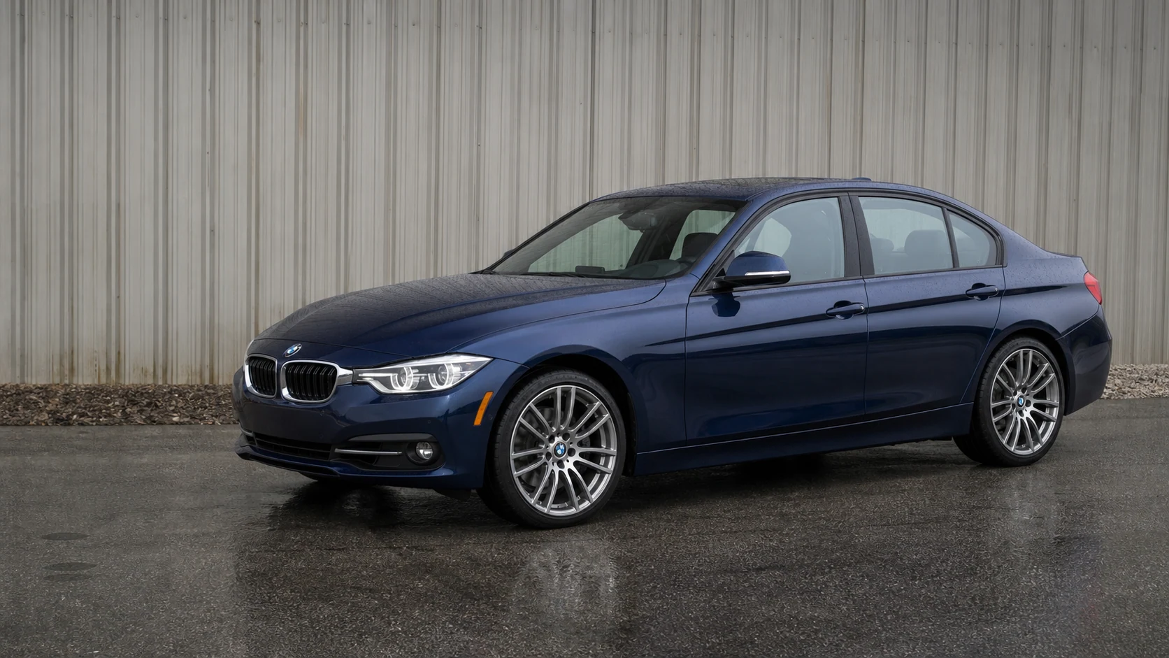 Blue F30 BMW 335i and 340i sedan on wet asphalt beside an industrial wall