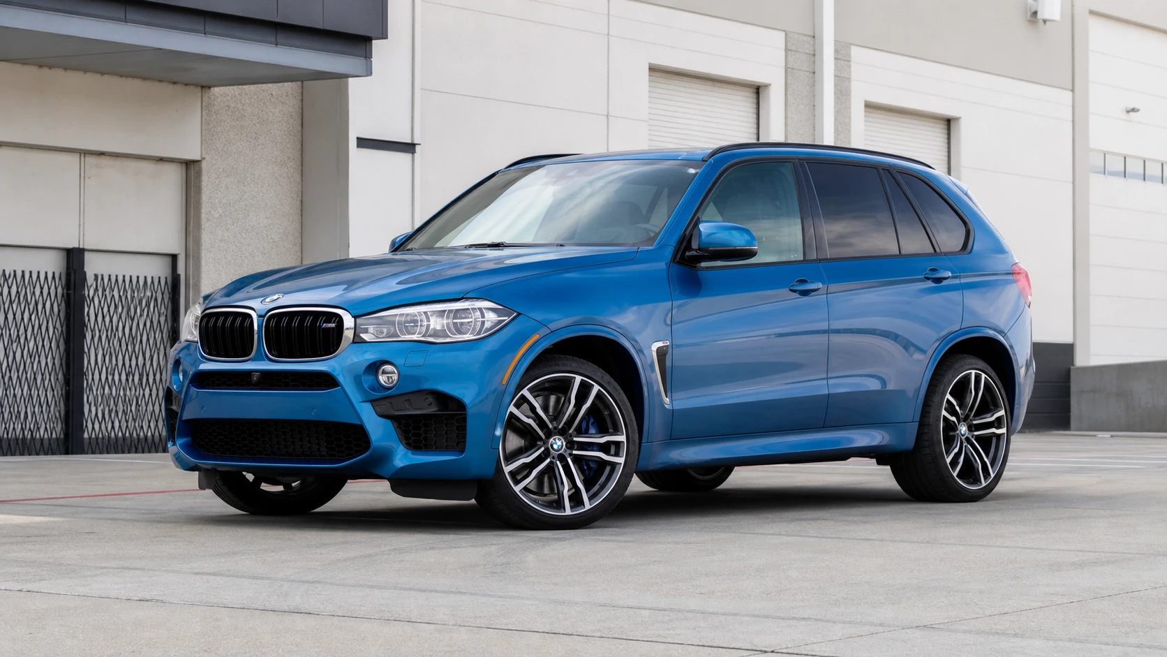 Blue F85 BMW X5 M outside an industrial warehouse