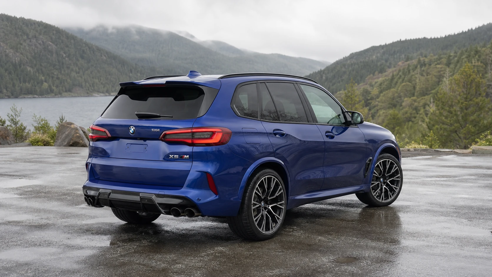 Blue F95 BMW X5 M in a rear three-quarter view at a misty mountain lake
