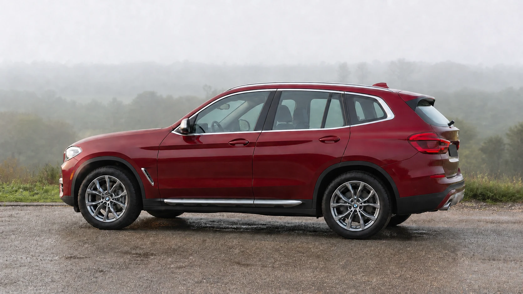 Burgundy G01 BMW X3 in side profile at a misty overlook