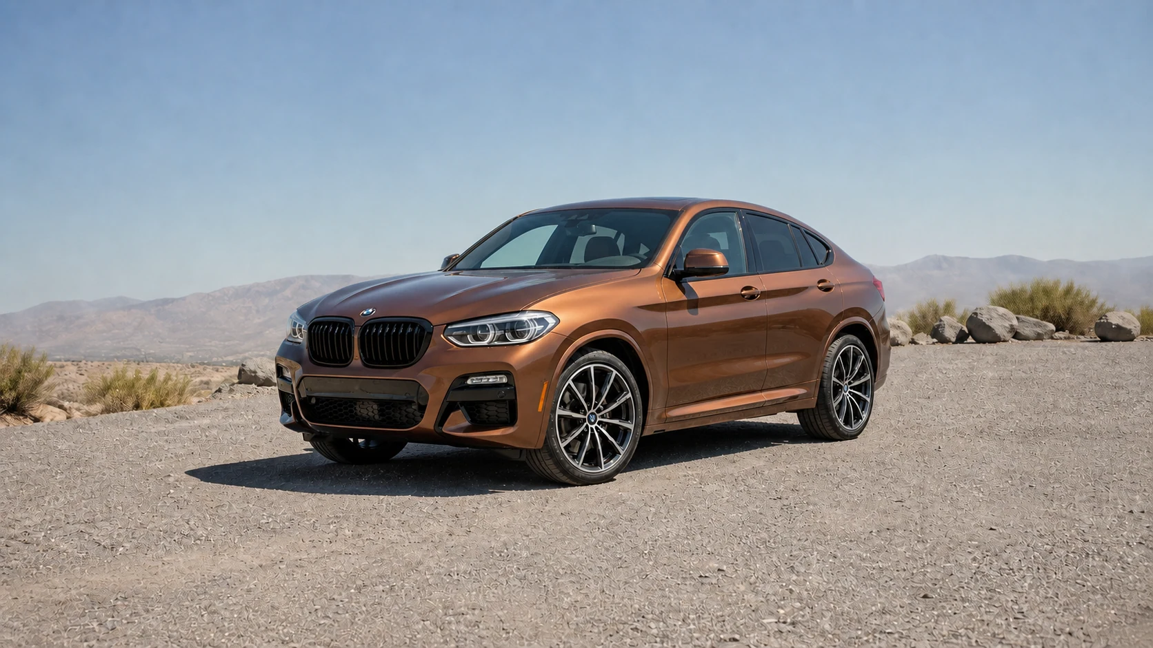 Copper-bronze G02 BMW X4 in a low front three-quarter view on open rocky terrain