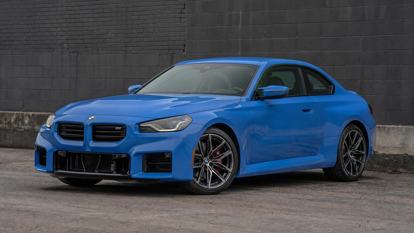Blue G87 BMW M2 coupe outside a charcoal industrial building