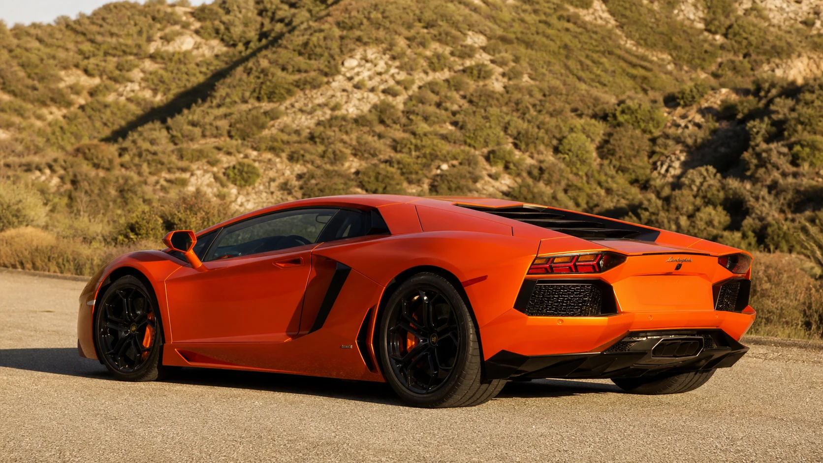 Orange Lamborghini Aventador in a rear three-quarter view at an alpine-scrub lay-by
