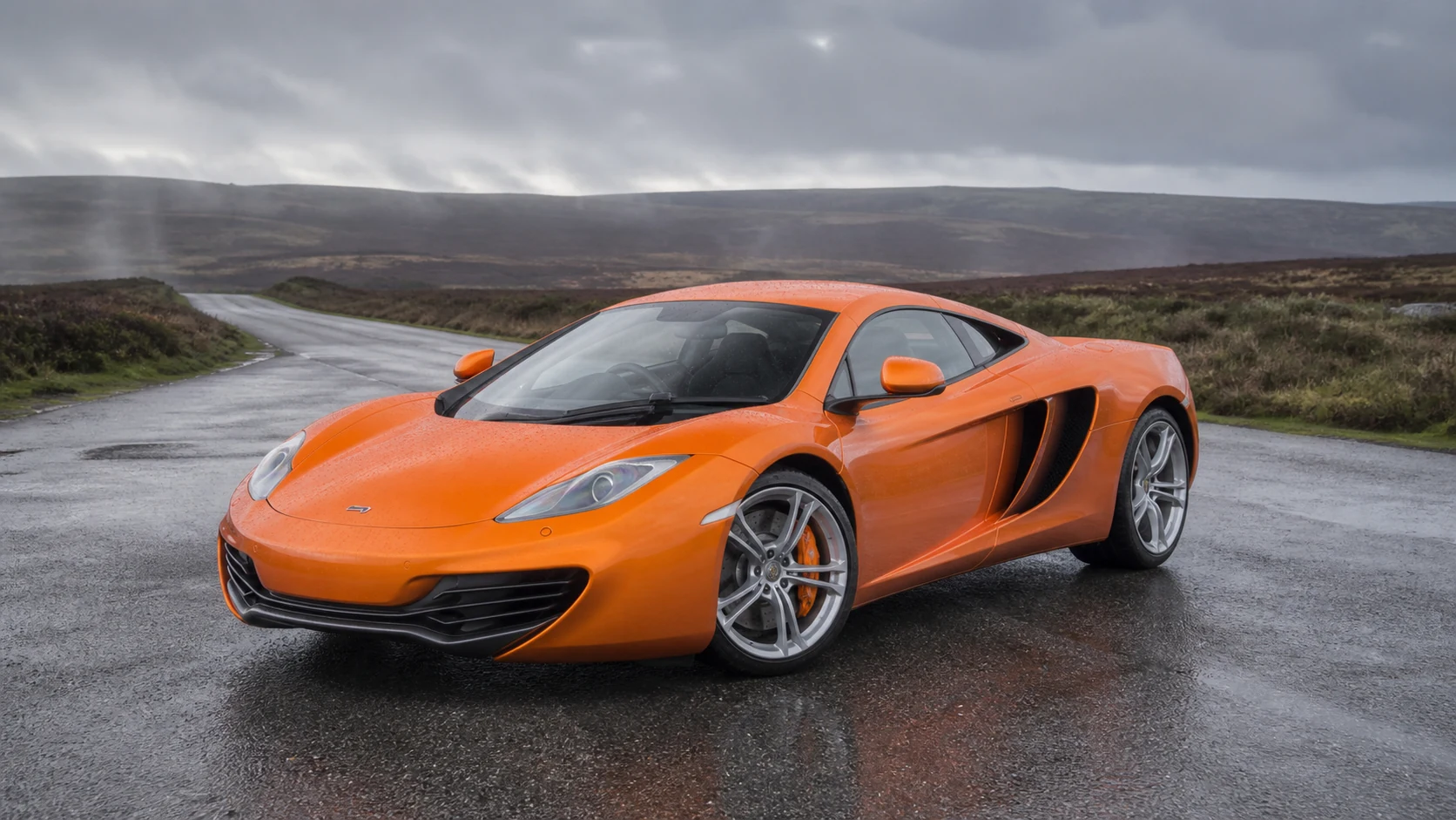 Orange McLaren MP4-12C on a rain-darkened moorland road