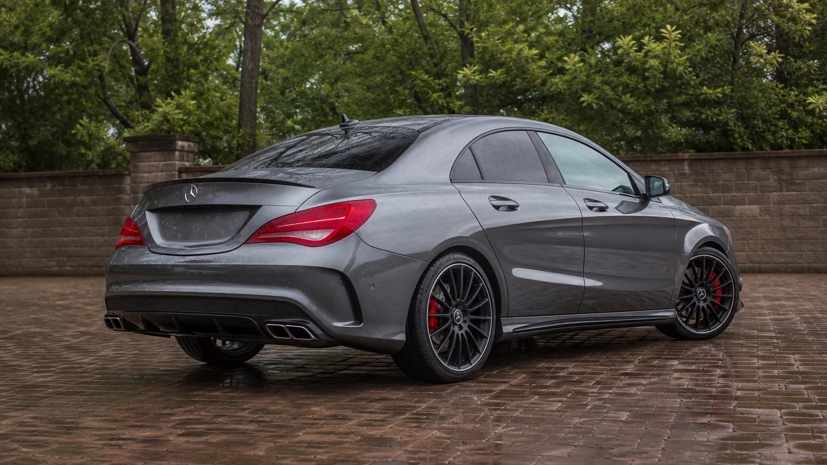 Gray C117 Mercedes-AMG CLA45 in a rear three-quarter view on a rain-damp brick courtyard