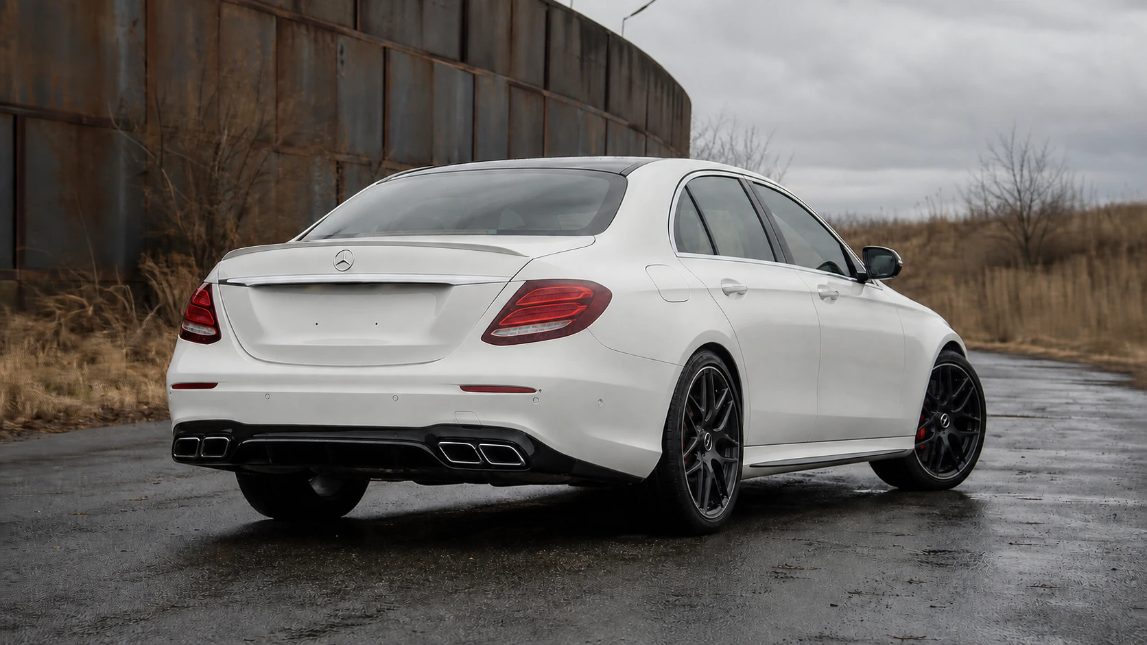 White 2017-2020 W213 Mercedes-AMG E63 in a rear three-quarter view on wet asphalt