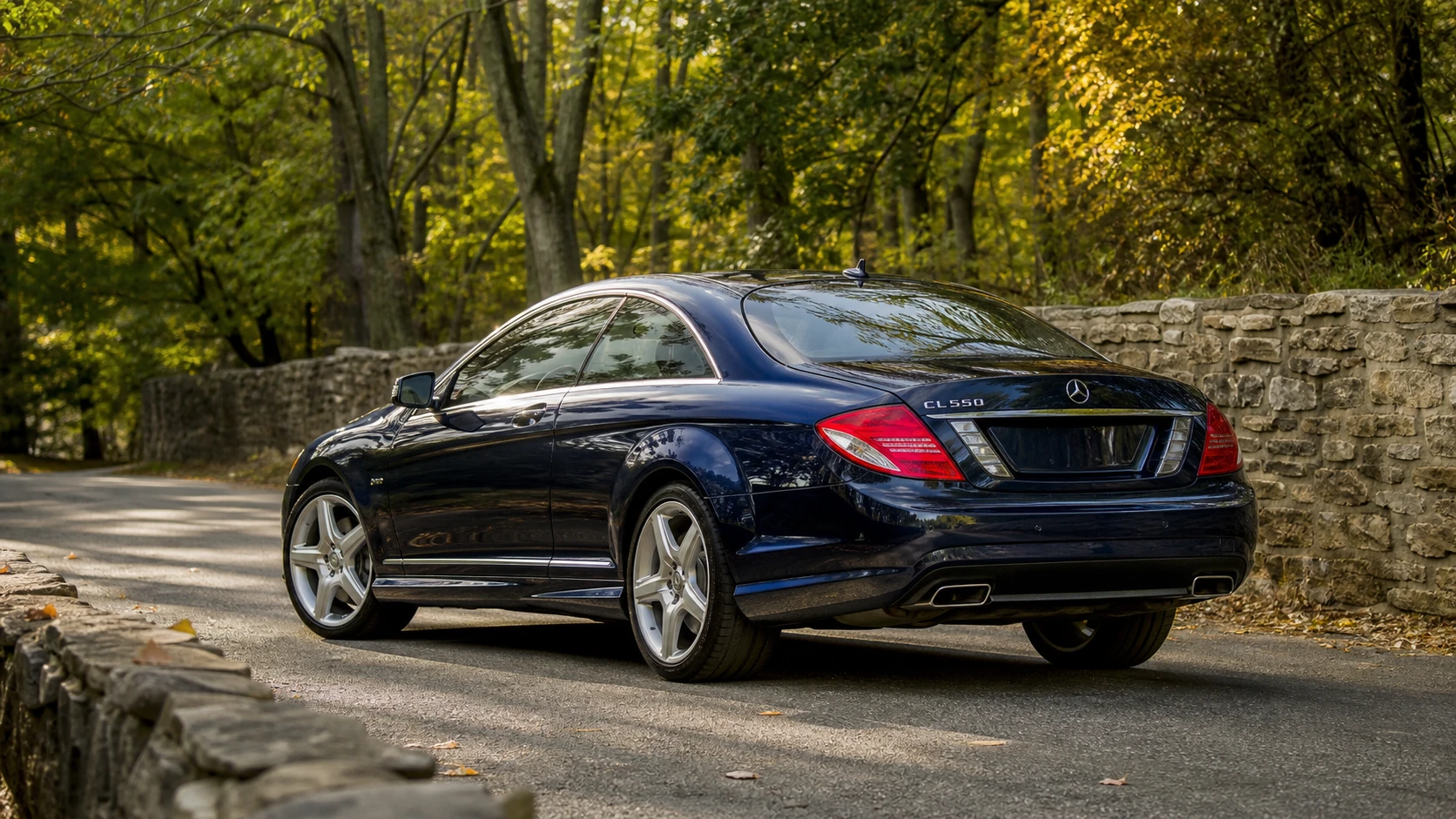 Blue Mercedes C216 CL550 coupe in a rear three-quarter view beside a stone wall